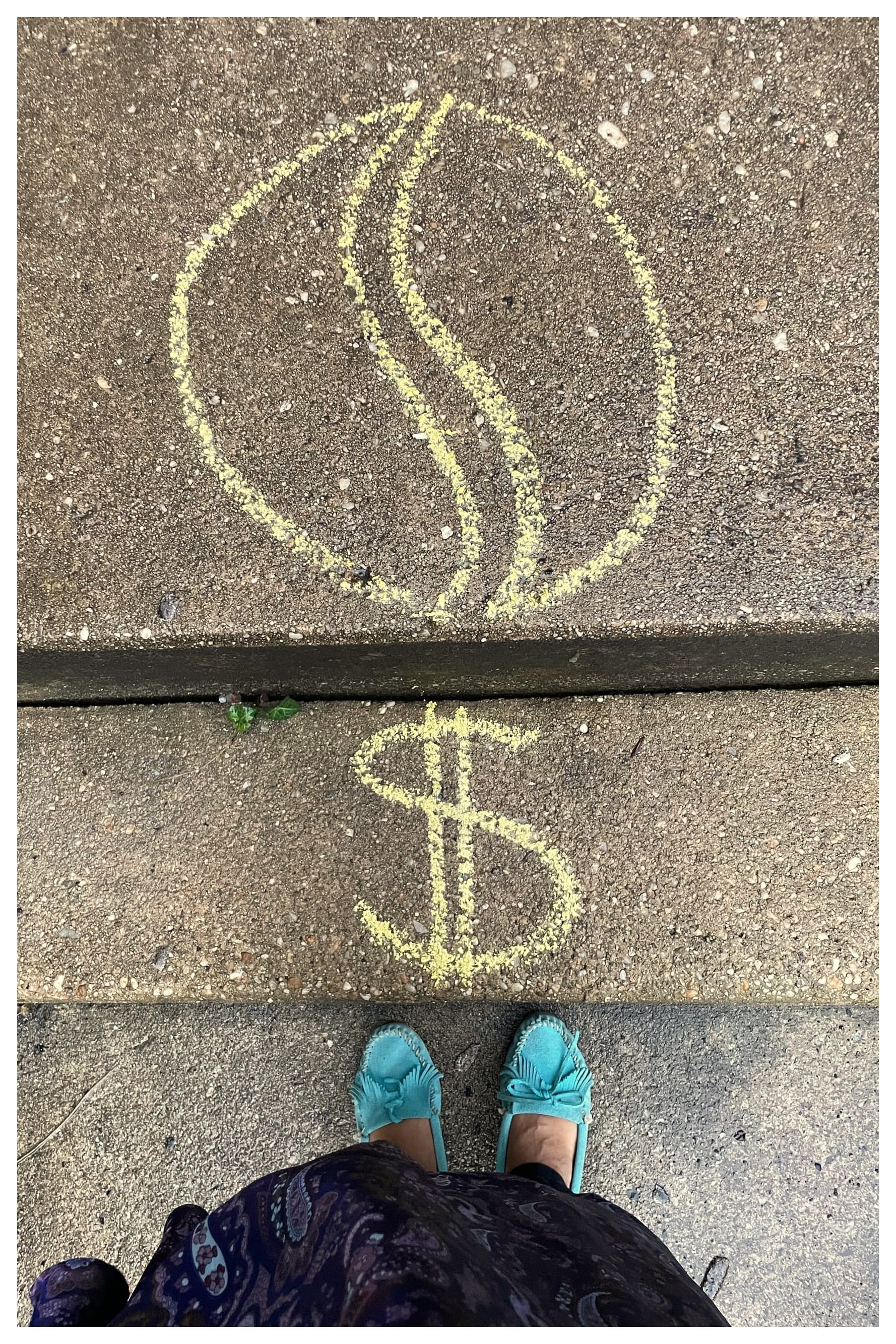 A brown-skinned person wearing turquoise moccasins and a purple paisley dress stands on wet pavement. A dollar sign drawn in